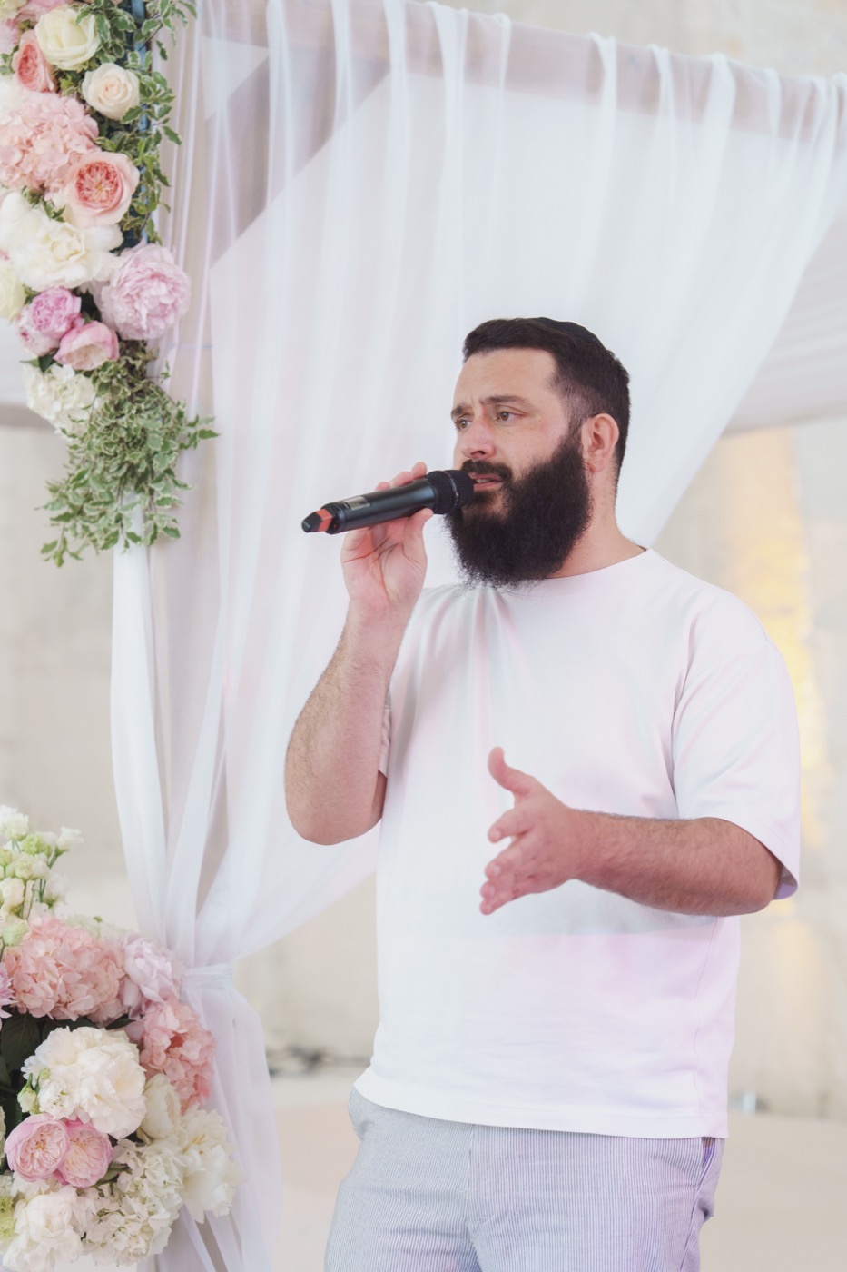 Chanteur barbu au micro devant des voilages blancs et des fleurs, Drop Music