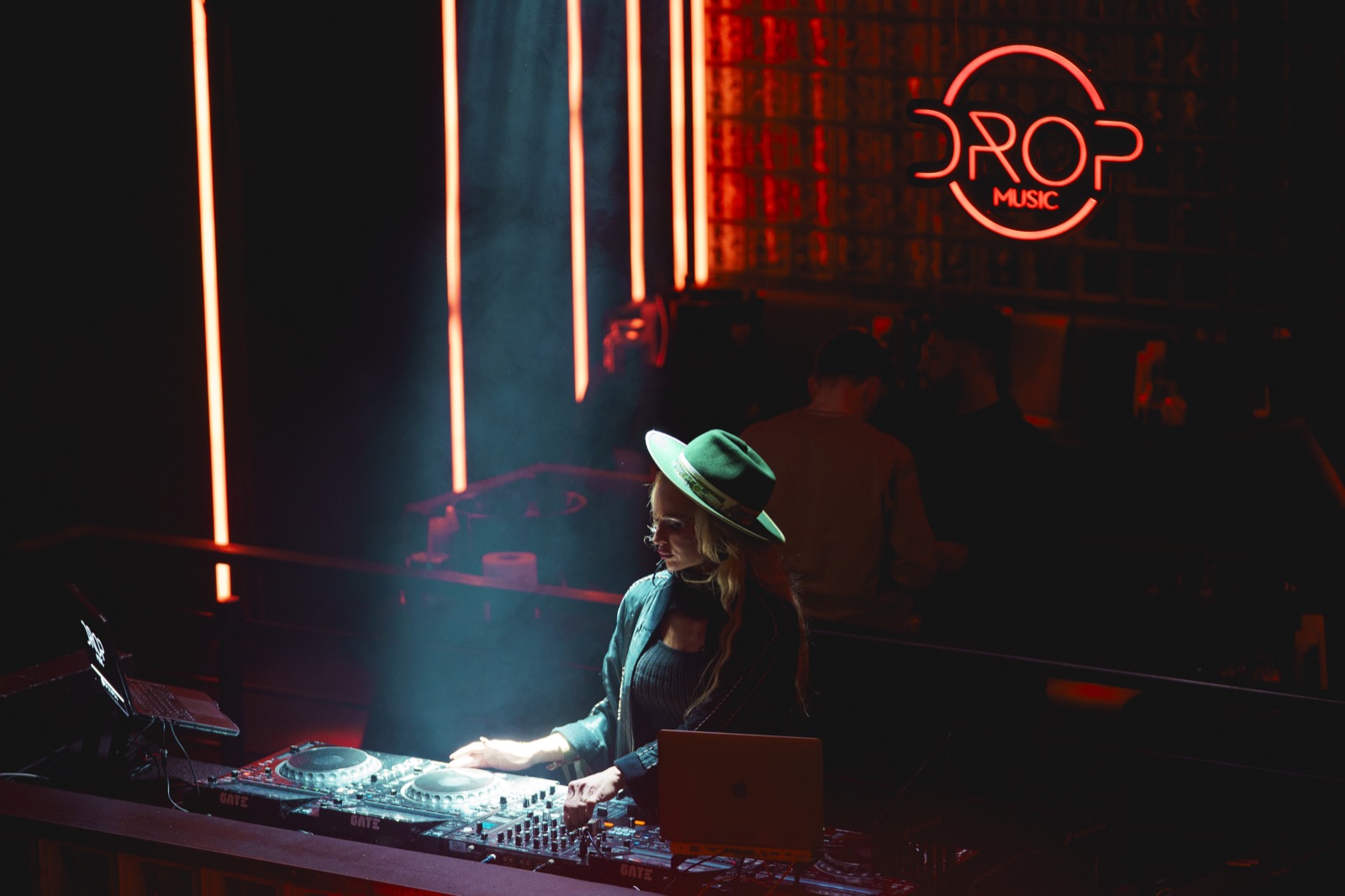 DJette au chapeau vert aux platines, logo Drop Music en néon rouge au-dessus, Drop Music