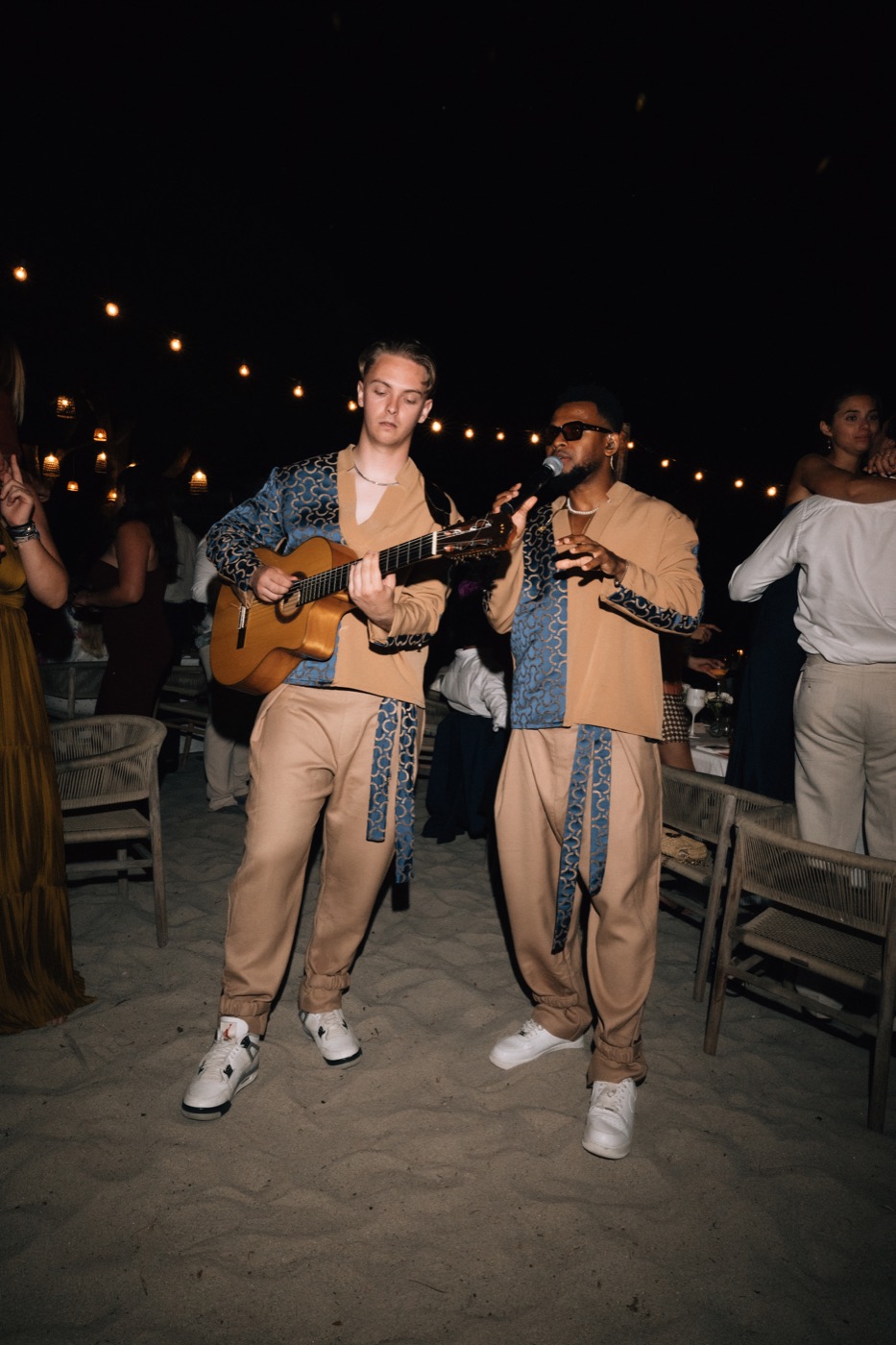 Guitariste et chanteur sur le sable, la nuit, entre les tables d’un dîner en plein air, Drop Music
