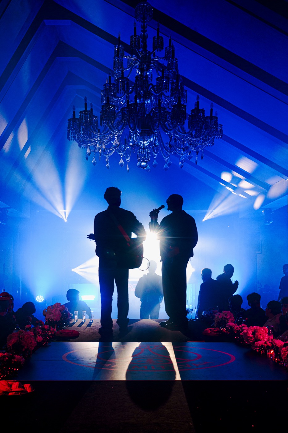Chanteur au micro au milieu des invités autour d’une table aux chandelles, Drop Music