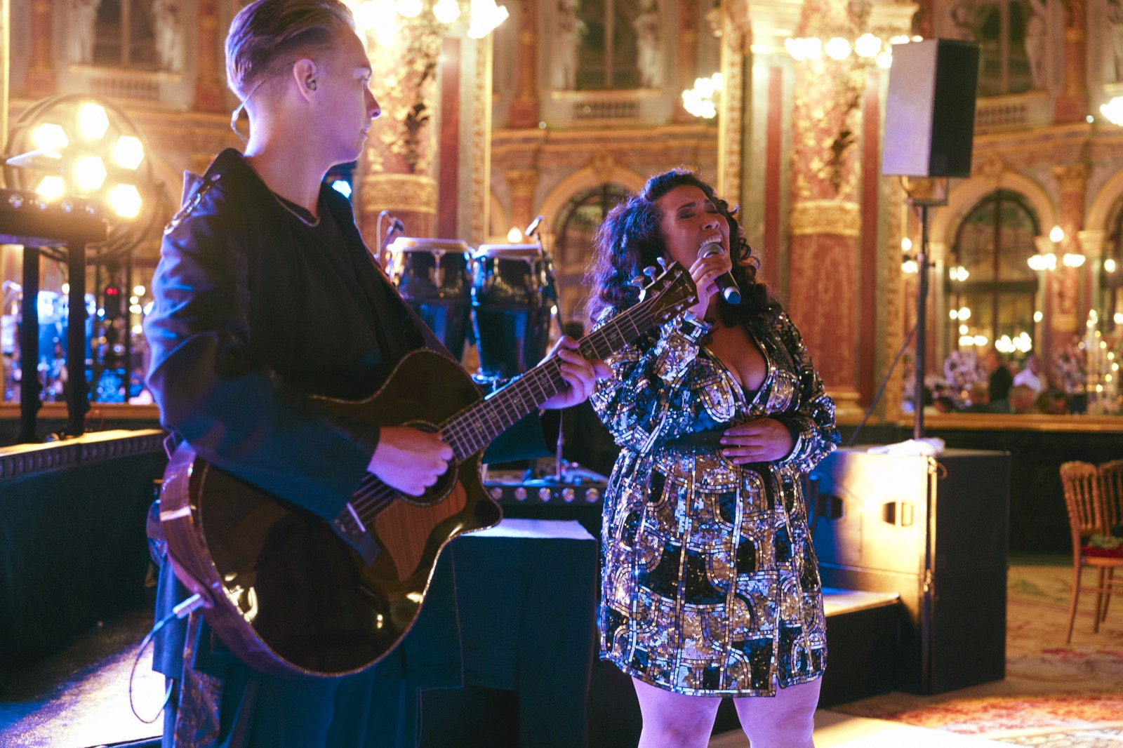 Guitariste et chanteuse en robe à sequins dans une salle de réception dorée, Drop Music