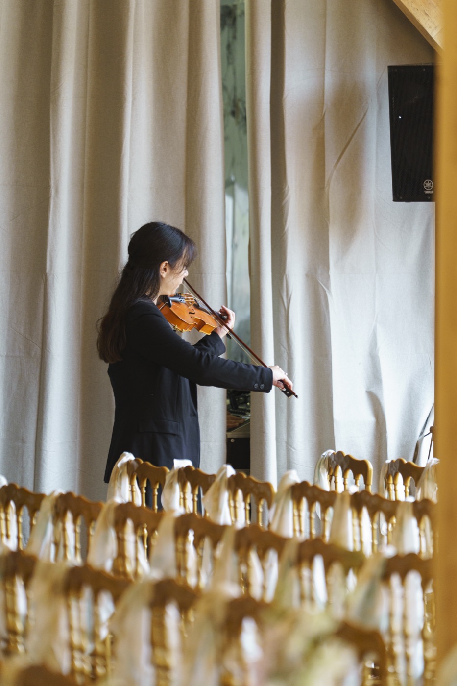 Violoniste devant les rangées de chaises dorées d’une cérémonie, voilages blancs, Drop Music