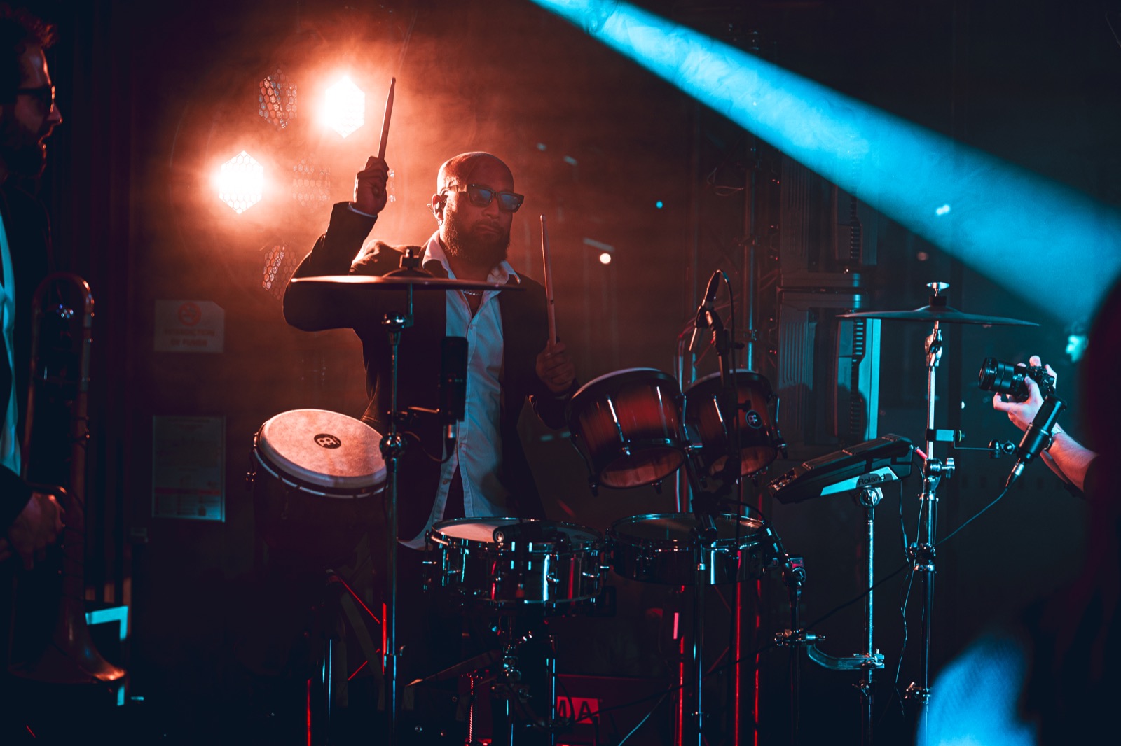Batteur baguette levée derrière sa batterie, lumière rouge et faisceau bleu, Drop Music