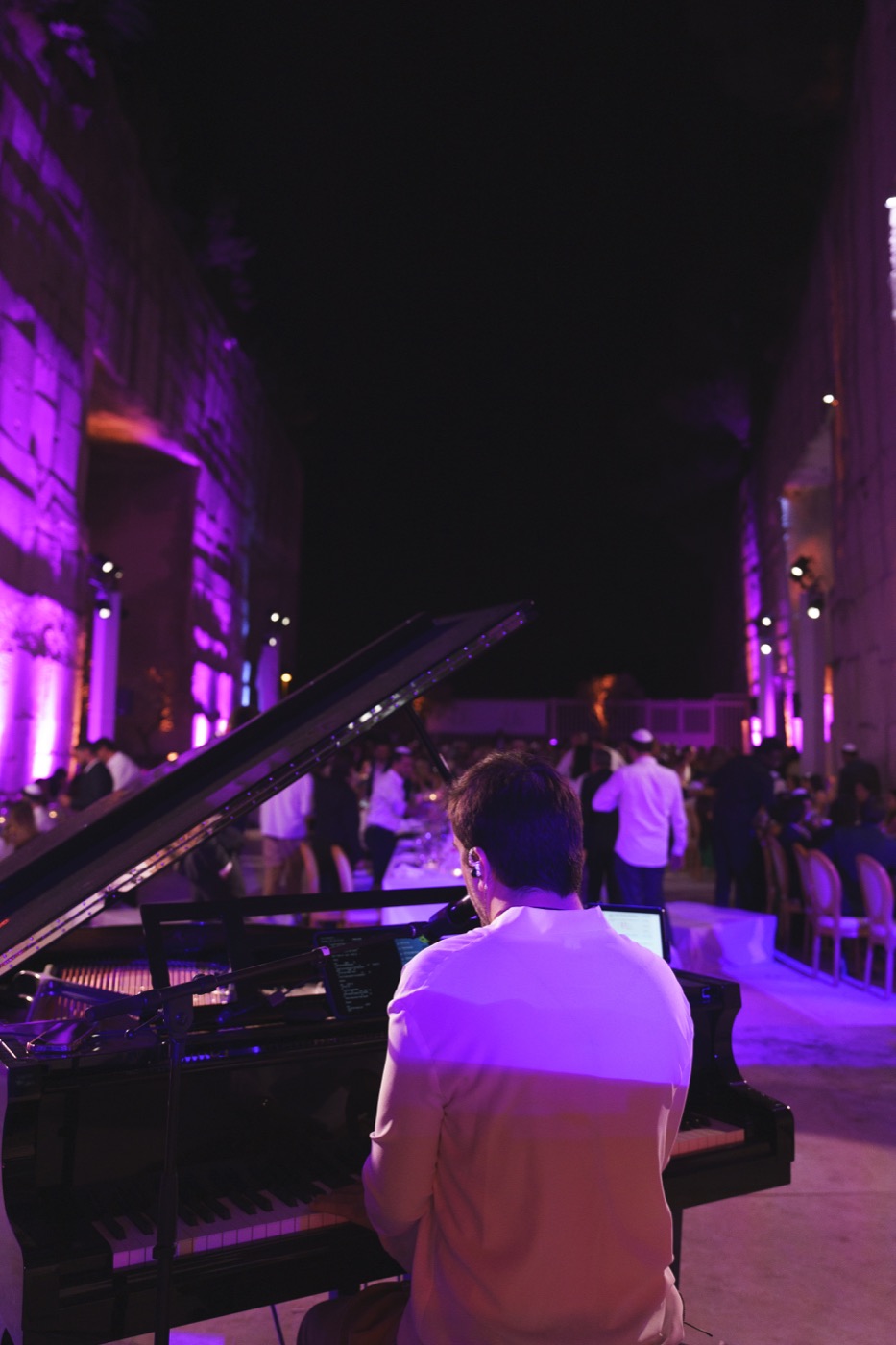 Pianiste de dos au piano à queue face aux invités, murs de pierre éclairés en violet, Drop Music