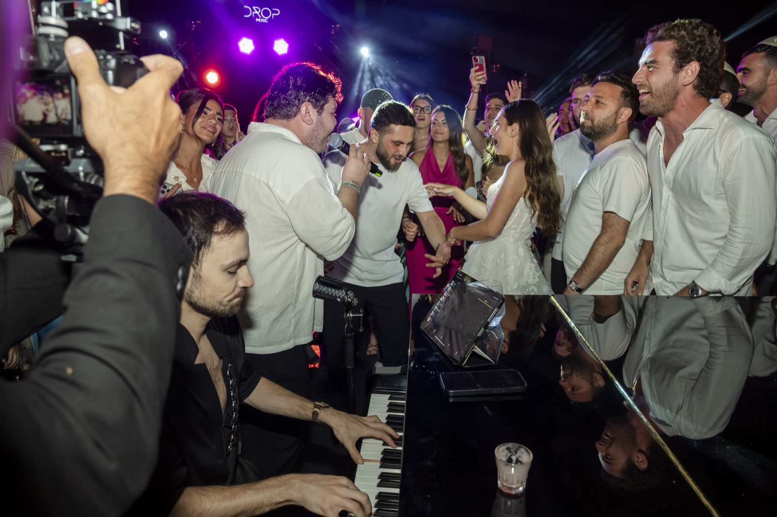 Pianiste au piano au milieu des invités qui dansent, caméraman au premier plan, Drop Music