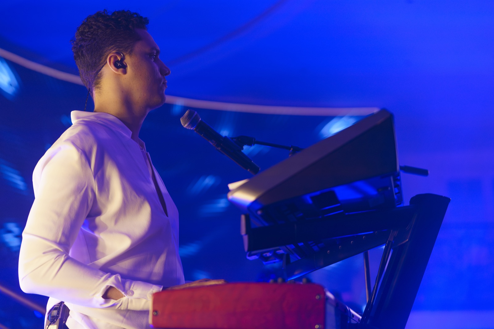 Chanteur au clavier sous une lumière bleue, oreillette en place, Drop Music