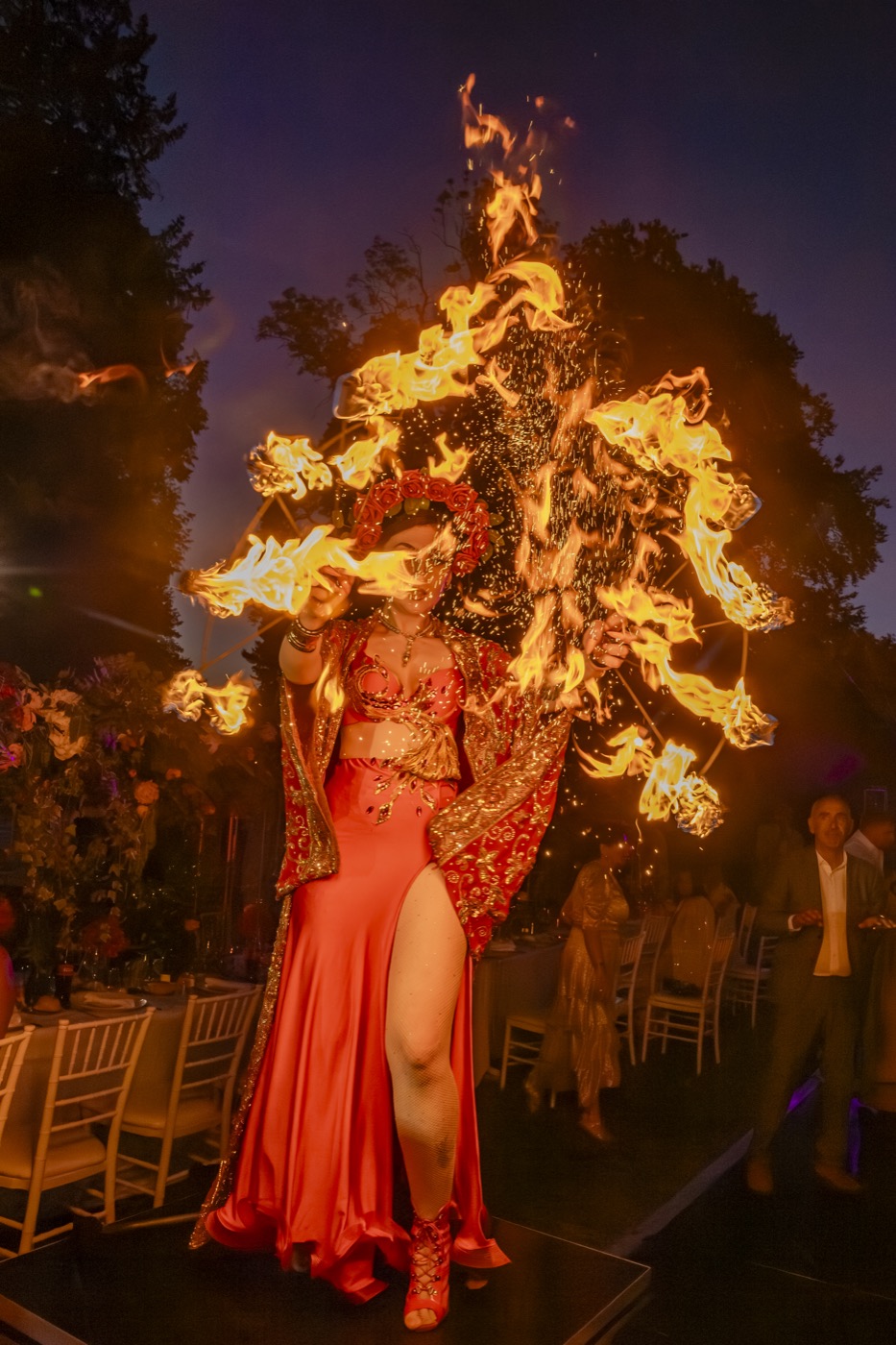 Performeuse en robe rouge et coiffe enflammée devant les invités, en extérieur, Drop Music