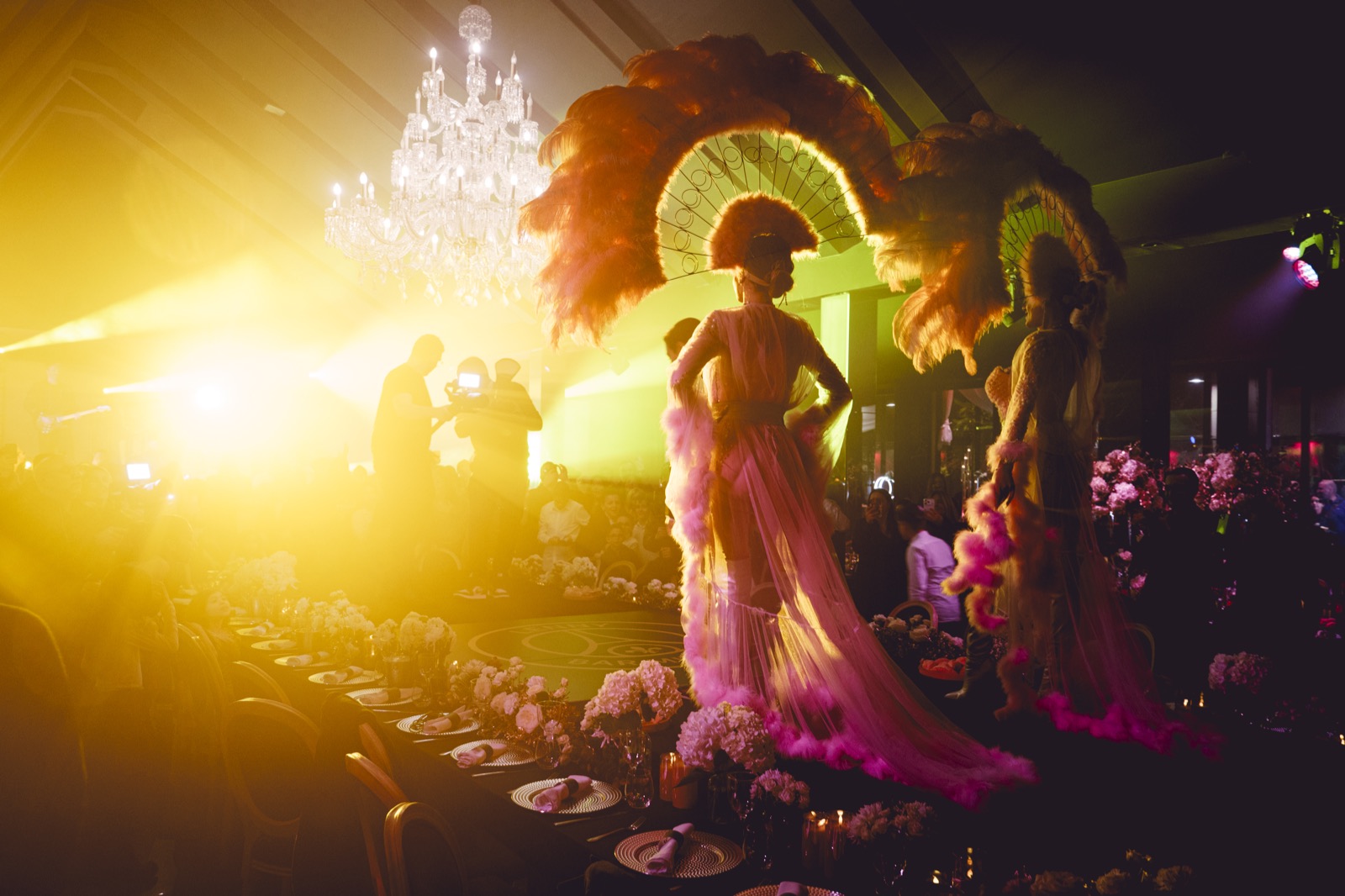 Performeuses en costume à plumes entre les tables, sous un lustre, Drop Music