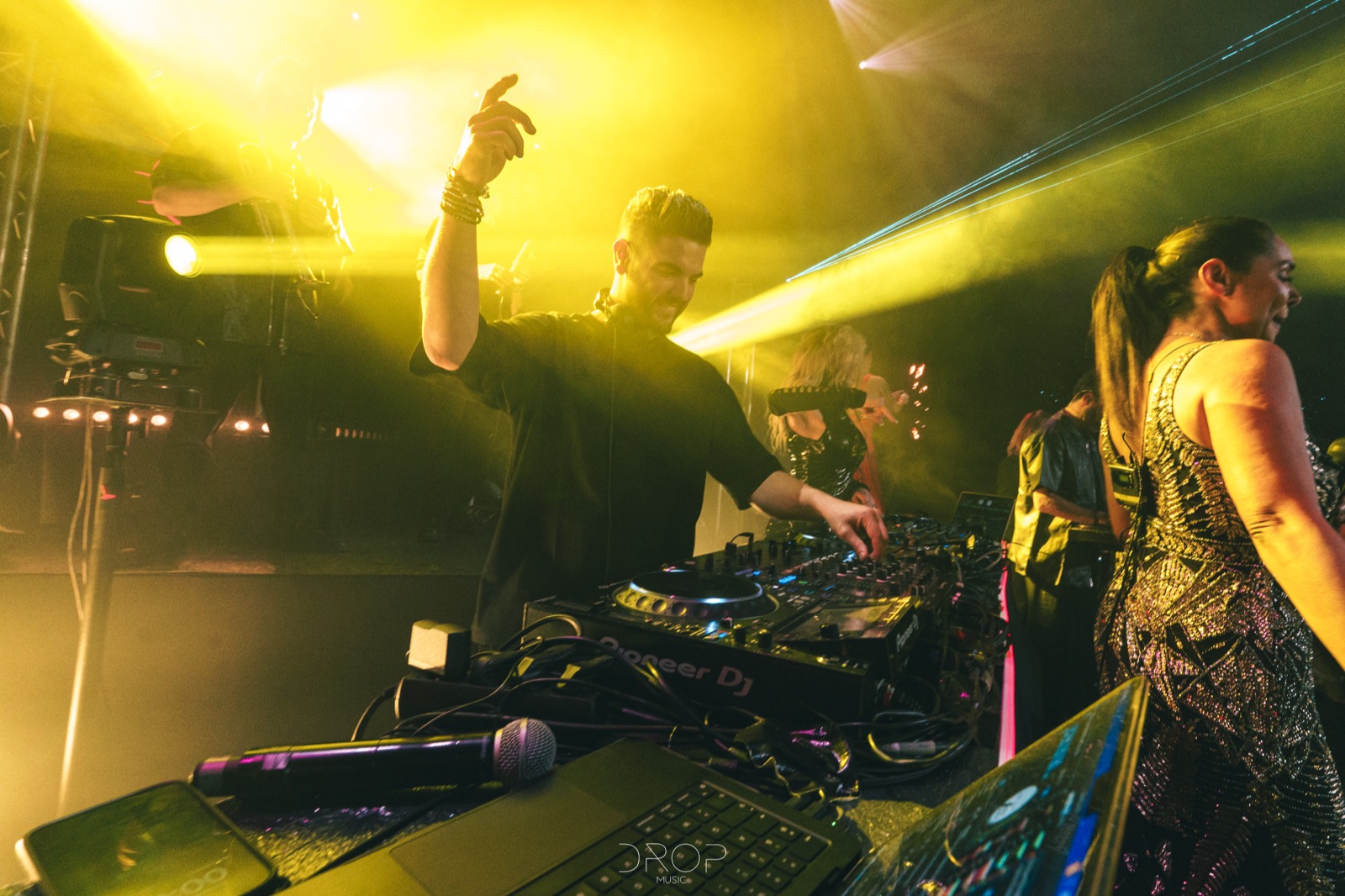 DJ seul aux platines, bras levé, au milieu des invités, Drop Music