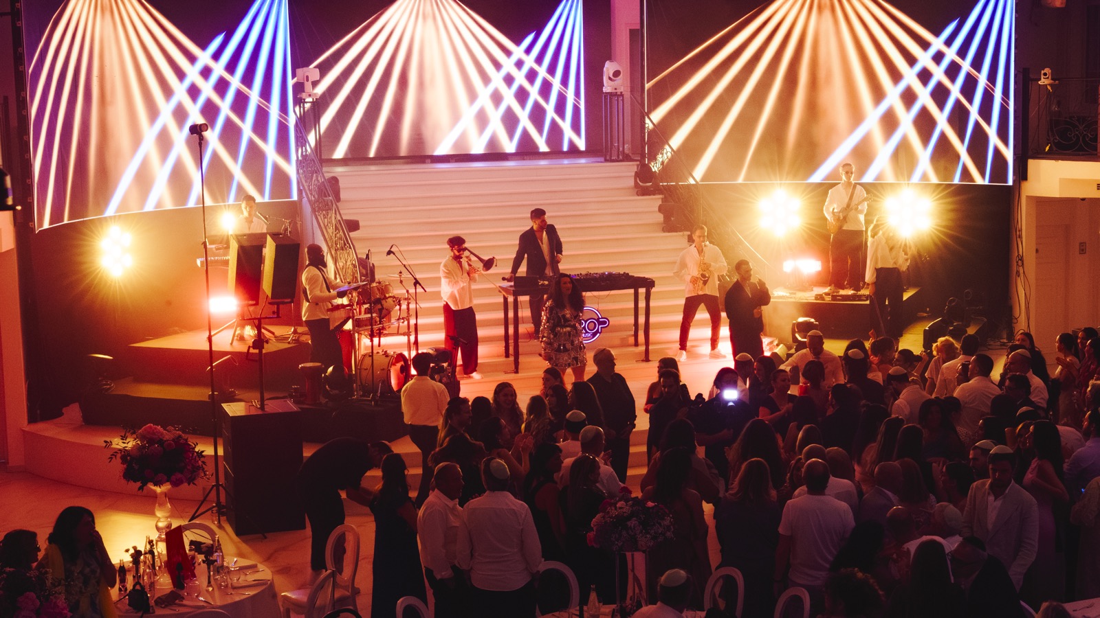 Orchestre live sur scène pendant un dîner, faisceaux blancs au-dessus des tables, Drop Music