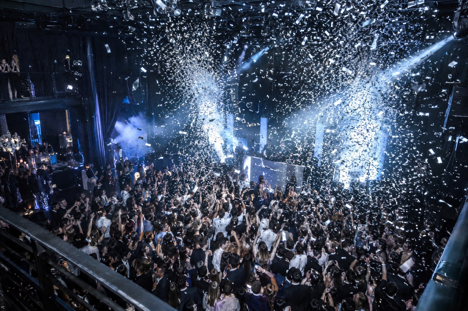 Pluie de confettis argentés sur une piste comble vue depuis la scène, faisceaux bleus au-dessus de la foule, Drop Music