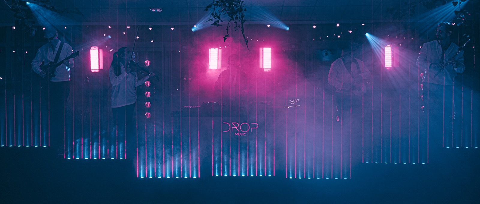 Barres lumineuses roses et faisceaux bleus dans la fumée au-dessus de la scène, logo Drop Music au fond, Drop Music