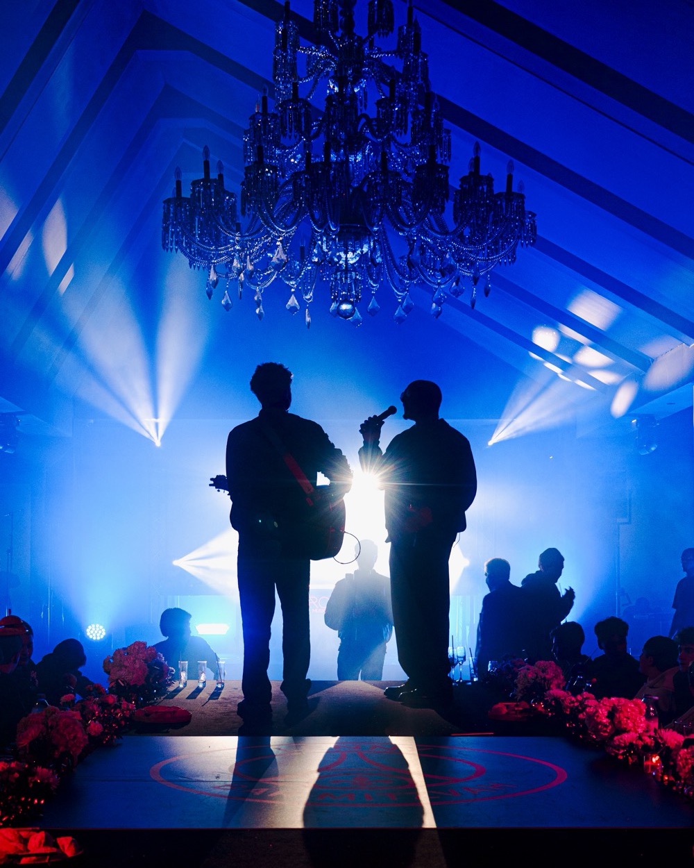 Guitariste et chanteur en contre-jour sur un riser, sous un lustre, pendant un dîner, Drop Music