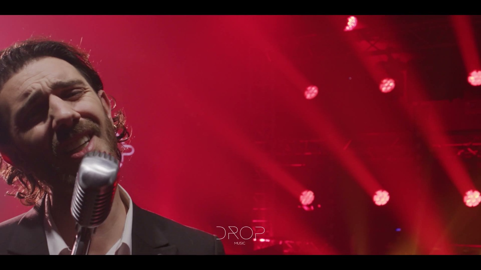 Chanteur en costume au micro sur pied, en lumière rouge, Drop Music