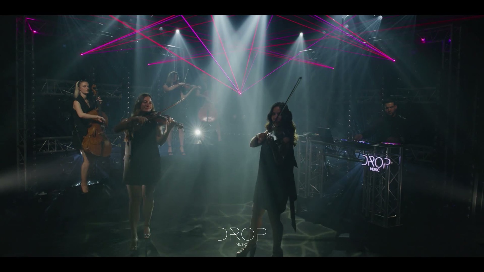 Trois violonistes debout sur scène, dans la fumée et les faisceaux, Drop Music